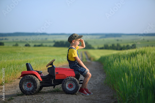 Little boy farmer on a tractor among green grain fields