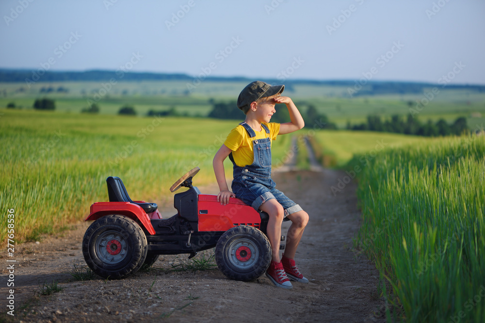 Little boy farmer on a tractor among green grain fields