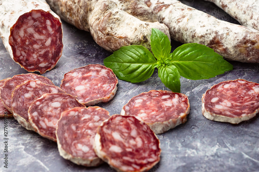 Traditional thin dried sausage with slices on grey stone background Traditional thin dried sausage with slices on grey stone background