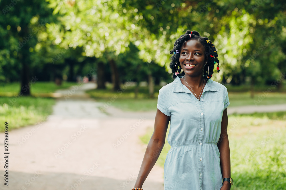 Portrait of a African beauty smiling young black woman in a park with sunlight flare and copy space