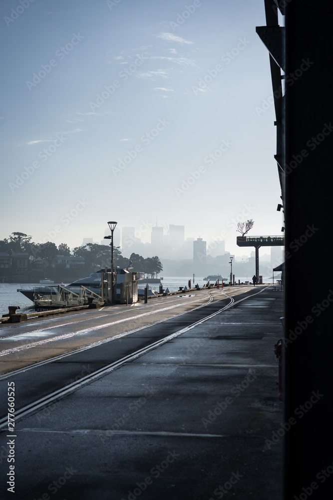 Low angle urbanscape at Jones Bay Wharf. North Sydney visibile in the through the early morning haze in the background. Sydney NSW. June 2019 Low angle urbanscape at Jones Bay Wharf. North Sydney visibile in the through the early morning haze in the background. Sydney NSW. June 2019
