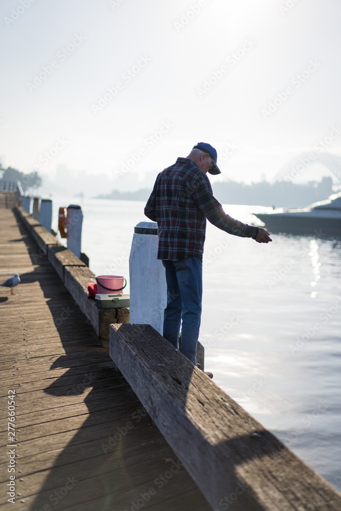 Local fisherman enjoys the early morning sun haze over the water at Pirrama Park/Jones Bay Wharf, Sydney NSW. June 2019
