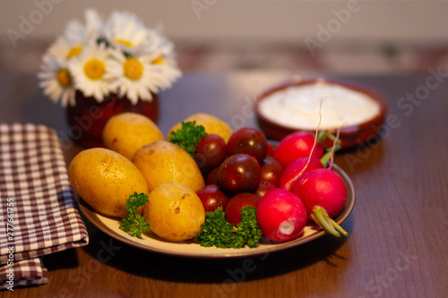 Cooked  upeeled potato  dark small tomato  radish  white sauce and bouquet of camomiles in vase on wooden table