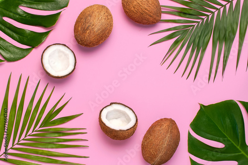 Frame of tropical leaves and fresh coconut on pink background. Flat lay, top view, copy space. Summer background, nature. Healthy cooking. Creative healthy food concept, half of coconut