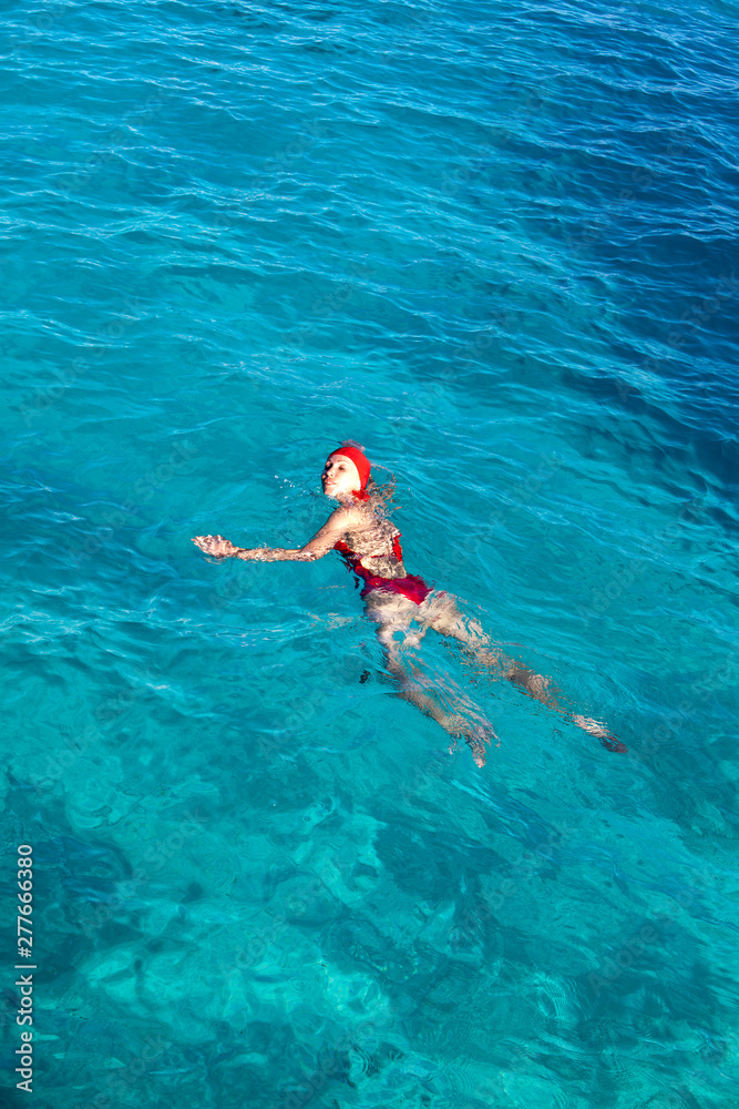 young woman in a red bathing suit swimming in the blue sea in Tahiti..