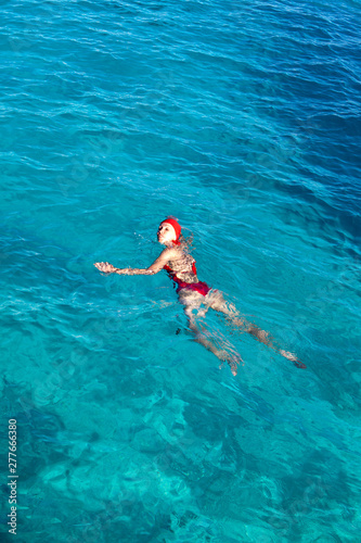 young woman in a red bathing suit swimming in the blue sea in Tahiti..