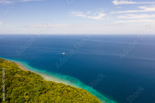 Green island with coral reef. Coast of Camiguin Island, Philippines, view from above. Seascape in sunny weather.