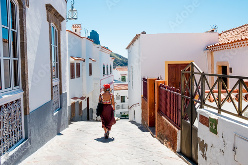 view of street inside small spanish town of Tejeda in gran canaria island with tourist woman walking on summer day with view of bentayga rock