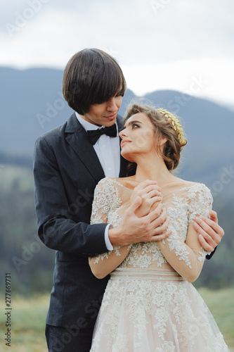 Bearded groom hugs blonde bride in a green garden with willows. Beautiful newlyweds kiss in a park with greenery. Wedding photography. photo