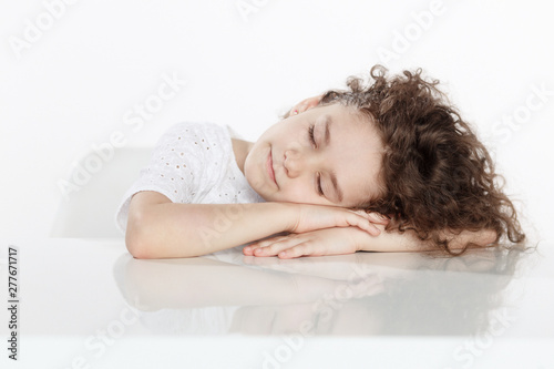 Adorable little curly girl sleeping paceful on a table  isolated on a white background. Horizontal view.