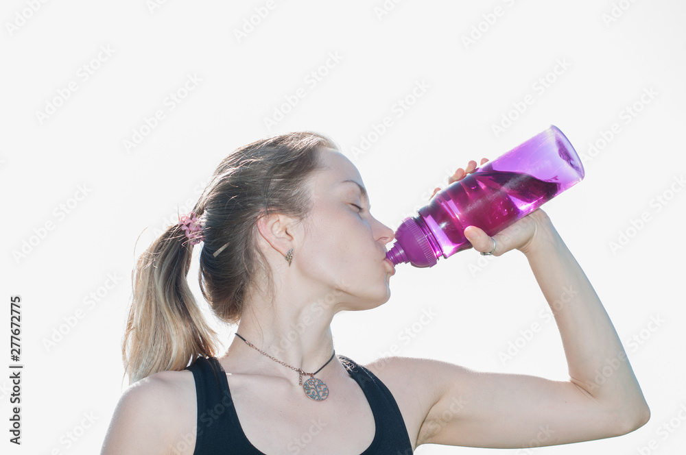 Young beautiful very pretty woman in a sporting suit drinks water from a bottle after workout in yoga, outdoor gymnastics in the summer Young beautiful very pretty woman in a sporting suit drinks water from a bottle after workout in yoga, outdoor gymnastics in the summer