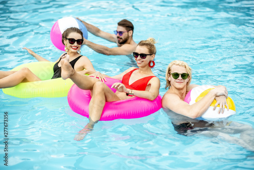 Group of a happy friends having fun, swimming with inflatable toys in the swimming pool outdoors during the summertime