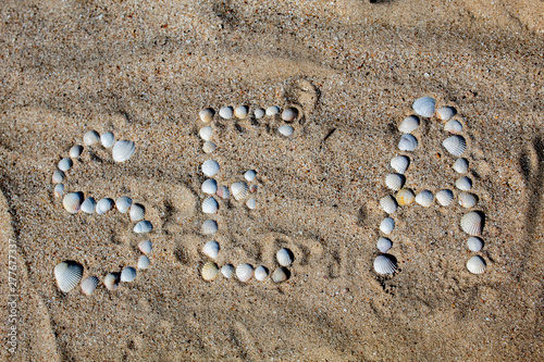 The word sea in English, laid out on the sand with shells. There is free space, space for text. Background.