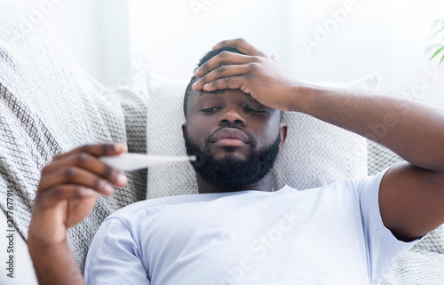 African-american man checking his body temperature at home