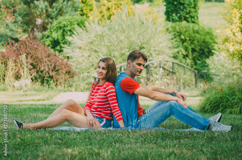 Young couple in love is sitting on the plaid in the park, back to back and enjoying the nature. Picnic for couples in love.