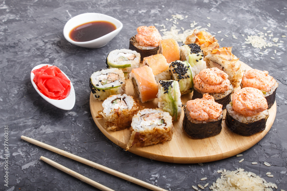 Mixed japanese maki sushi rolls set with chopsticks, ginger, soy sauce,rice on black concrete background, side view.