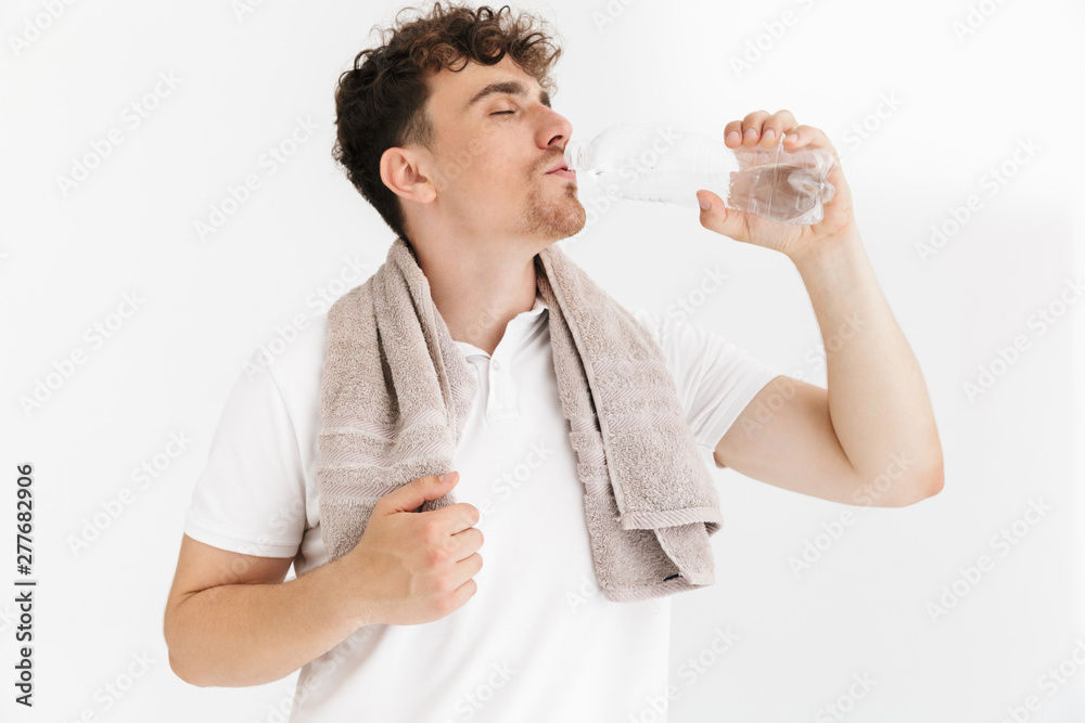 Photo closeup of caucasian young man with towel drinking water from plastic bottle after workout Photo closeup of caucasian young man with towel drinking water from plastic bottle after workout