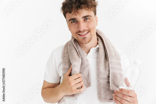Photo closeup of positive man with towel smiling at camera and holding water bottle