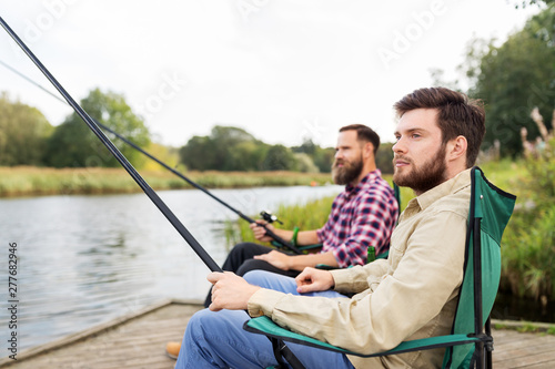 leisure and people concept - male friends with fishing rods on lake