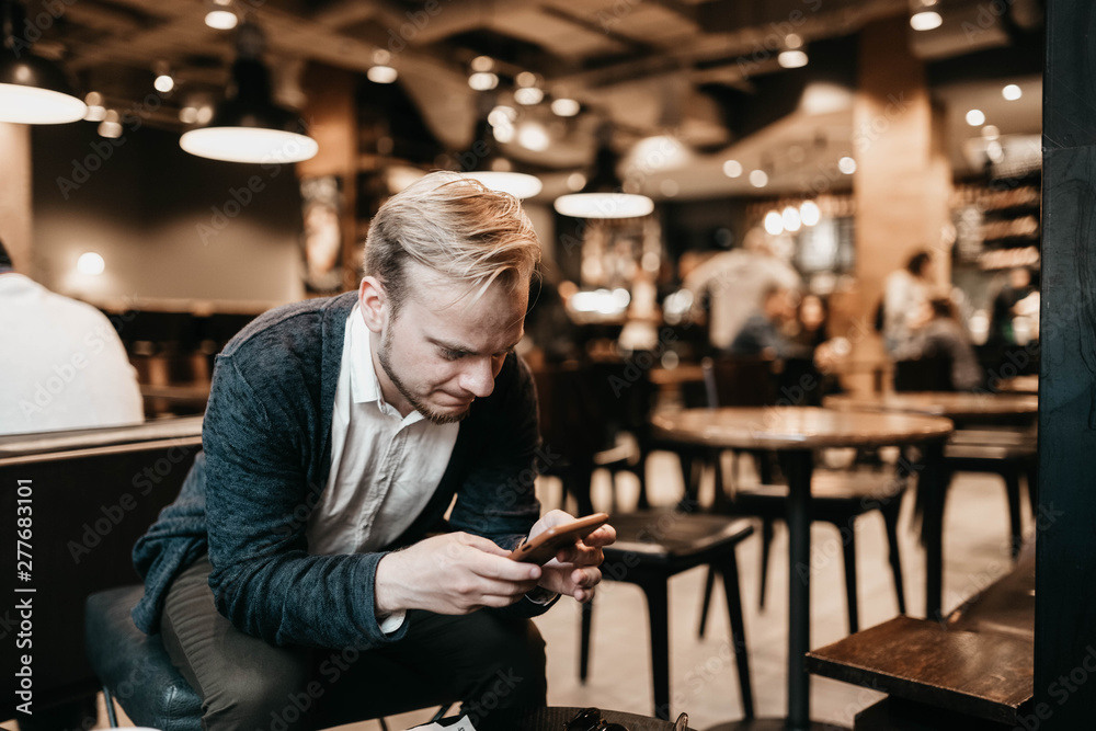 european male businessman with glasses uses a smartphone in a coworking cafe with a warm cozy light