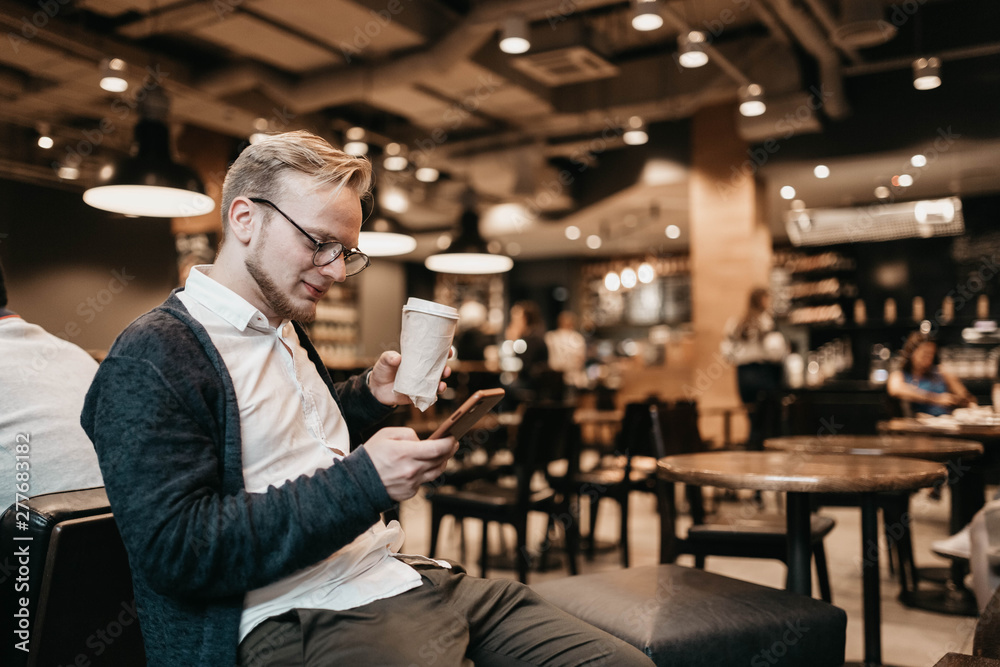 Male businessman with smartphone and coffee in coworking cafe. Cozy place for freelancer.