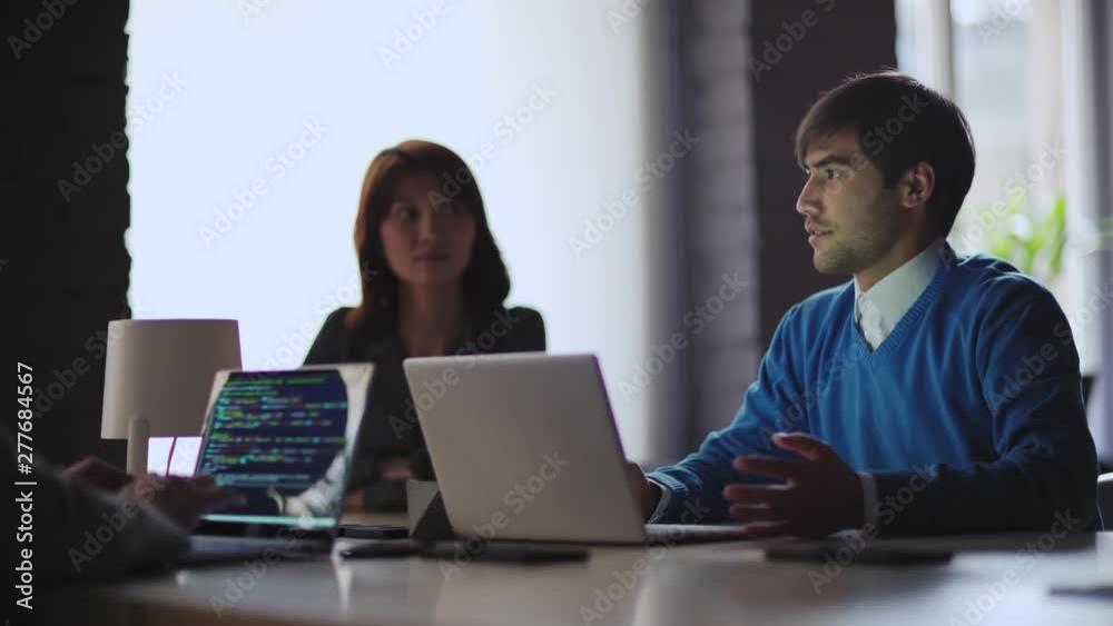 Team of four young business people planning online startup at meeting. Focus on smiling Middle Eastern man explaining his ideas. Female programmer coding on laptop, tracking shot