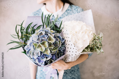 Very nice young woman holding beautiful tender blossoming mono bouquets of fresh white and blue hydrangea flowers and eucalyptus on the grey wall background photo