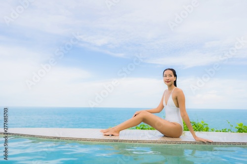 Portrait young asian woman relax smile happy around outdoor swimming pool in hotel resort with sea ocean view