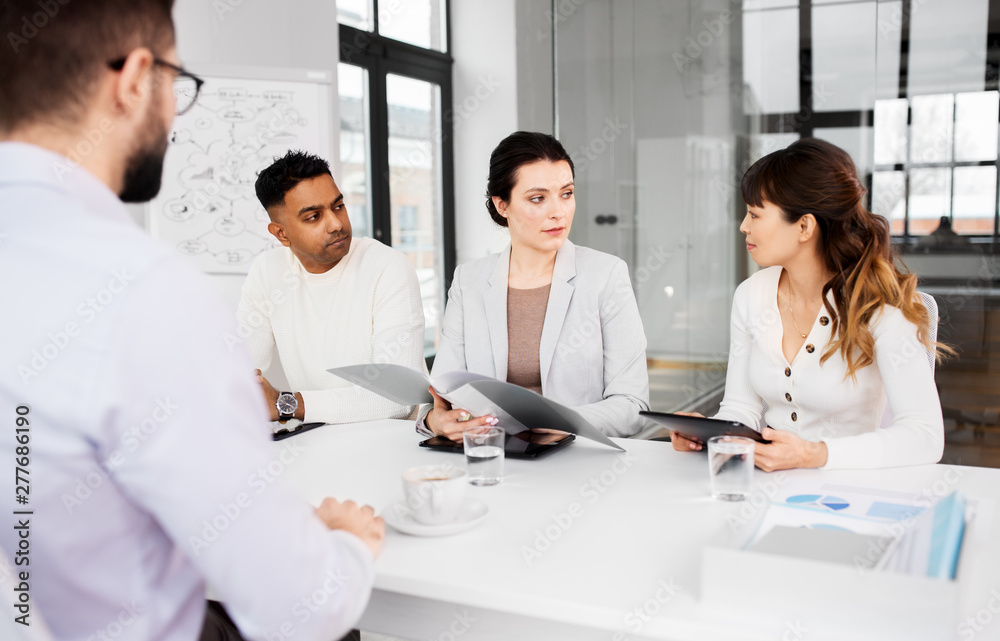 new job, hiring and employment concept - international team of recruiters with tablet computer and folder having interview with male employee at office new job, hiring and employment concept - international team of recruiters with tablet computer and folder having interview with male employee at office