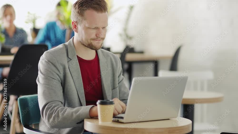 Tracking shot of middle aged businessman sitting at table in cafe, working on laptop computer and experiencing some difficulties Tracking shot of middle aged businessman sitting at table in cafe, working on laptop computer and experiencing some difficulties