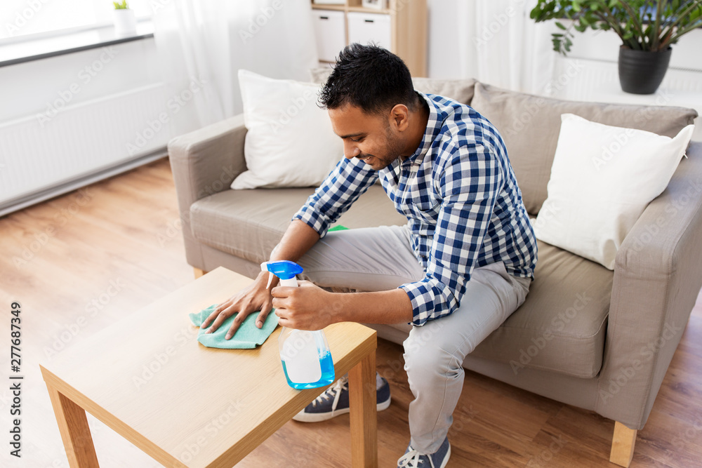 household and people concept - indian man with detergent cleaning table by rag at home household and people concept - indian man with detergent cleaning table by rag at home