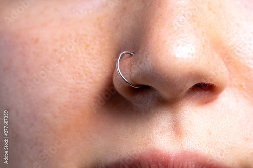 A closeup view on the pierced nose of a beautiful Caucasian woman. Front view showing details of a small silver nose-ring piercing the alae.