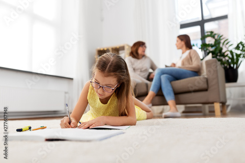 education, school and learning concept - student girl lying on floor and writing to notebook at home