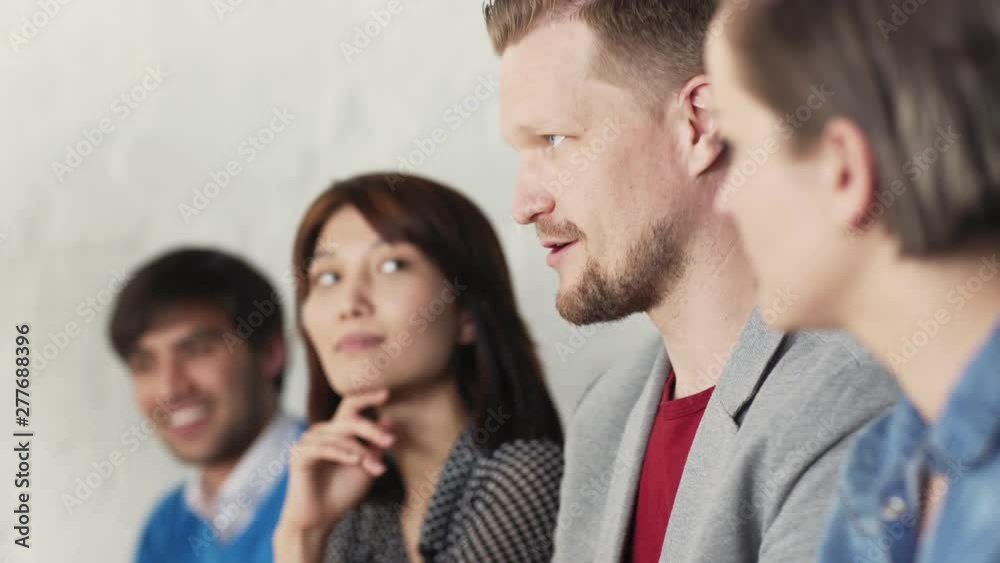 Tracking shot closeup of multi-ethnic business people sitting at conference during presentation and listening to colleague telling stories. Selective focus on middle aged man talking Tracking shot closeup of multi-ethnic business people sitting at conference during presentation and listening to colleague telling stories. Selective focus on middle aged man talking