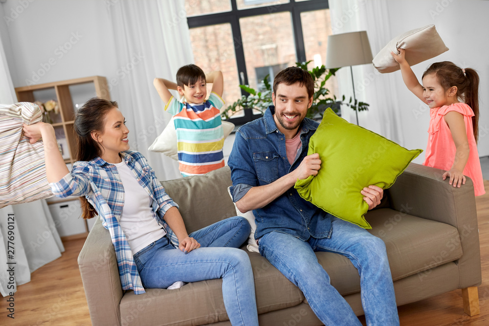 family, childhood and people concept - happy father, mother, little son and daughter fighting by pillows and having fun at home family, childhood and people concept - happy father, mother, little son and daughter fighting by pillows and having fun at home