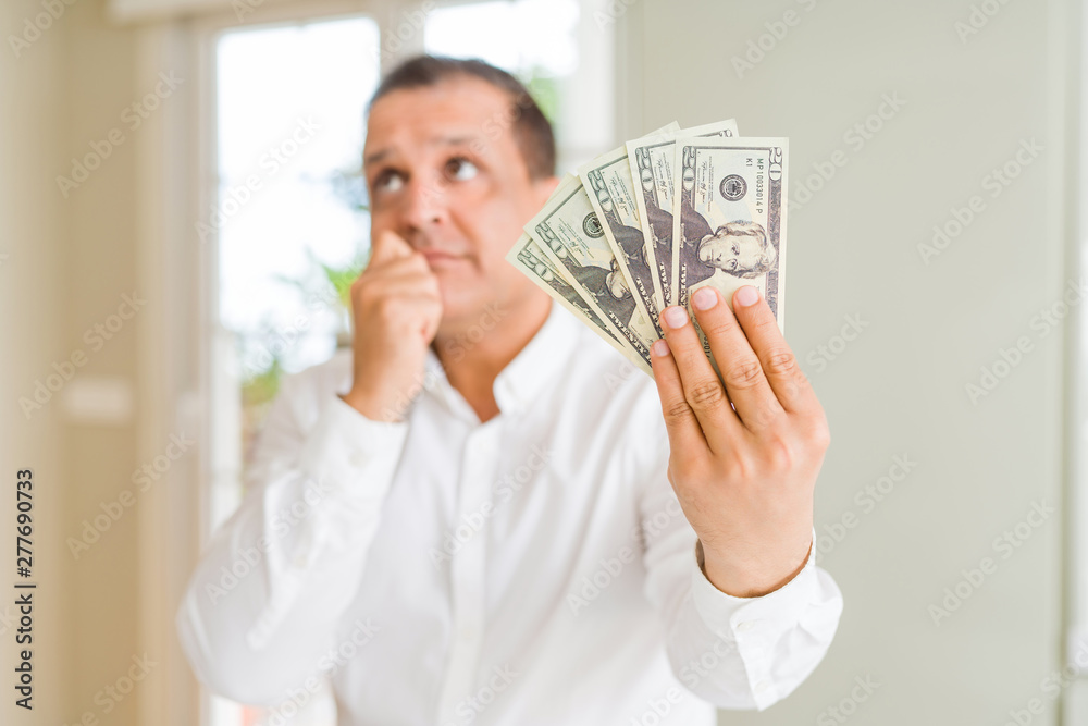 Middle age man holding bunch of dollars serious face thinking about question, very confused idea Middle age man holding bunch of dollars serious face thinking about question, very confused idea