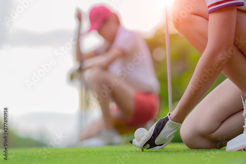 hand of young woman golf player holding golf ball laying on wooden tee, prepare and ready to hit the ball to the destination target, opponent competitor or golf mate buddy watching in background photo