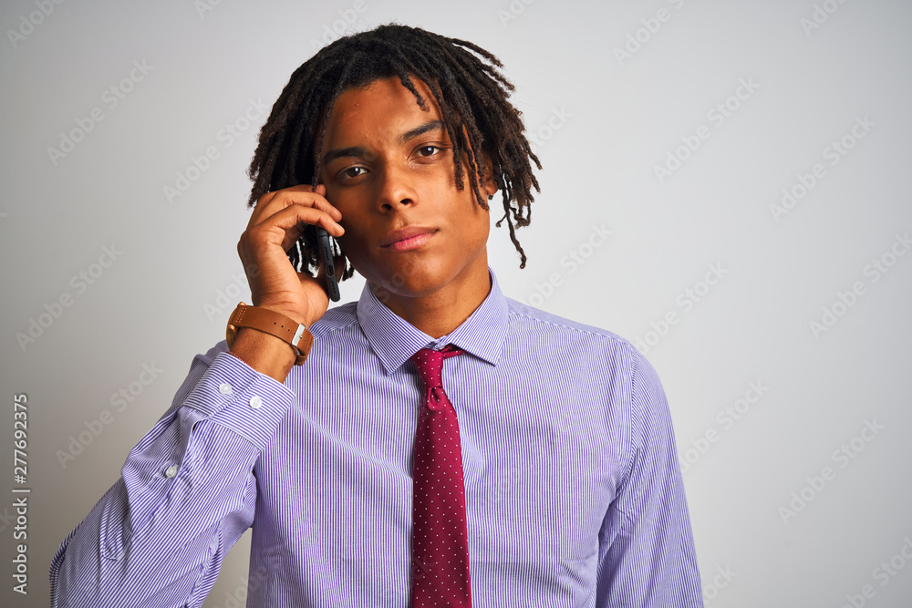 Afro businessman with dreadlocks talking using smartphone over isolated white background with a confident expression on smart face thinking serious Afro businessman with dreadlocks talking using smartphone over isolated white background with a confident expression on smart face thinking serious