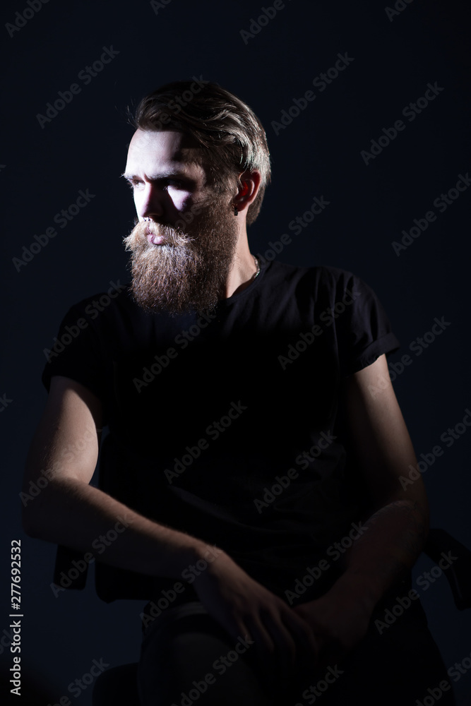stylish bearded man in a black t-shirt sitting in a chair
