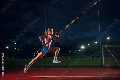 Ready to overcome difficulties. Professional female pole vaulter training at the stadium in the evening. Practicing outdoors. Concept of sport, activity, healthy lifestyle, action, movement, motion. photo