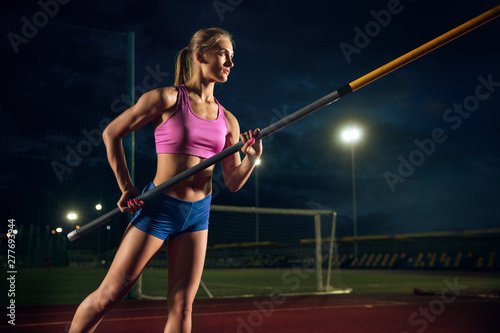Ready to overcome difficulties. Professional female pole vaulter training at the stadium in the evening. Practicing outdoors. Concept of sport, activity, healthy lifestyle, action, movement, motion. © master1305