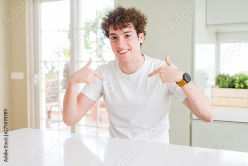 Young handsome man wearing white t-shirt at home looking confident with smile on face  pointing oneself with fingers proud and happy.