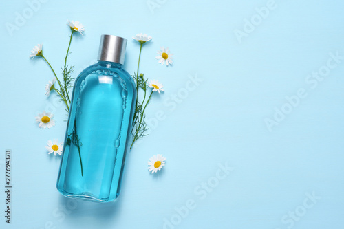 Cosmetic bottle and chamomile flowers on blue table top view with text space