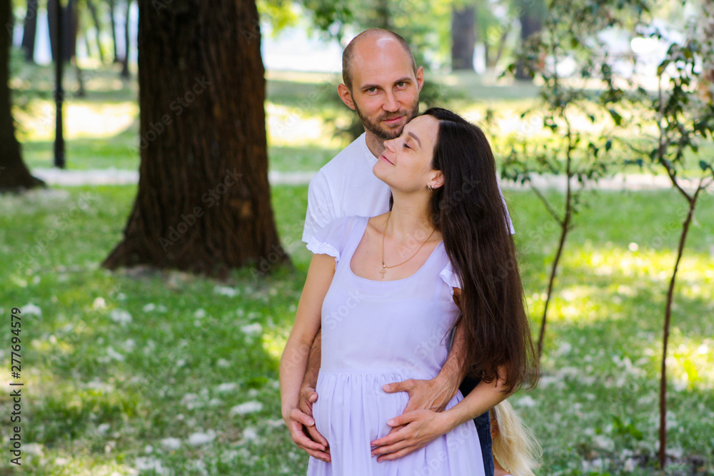 Fototapeta premium Portrait of happy loving couple hugging tenderly and warmly in the park and expecting the arrival of newborn.
