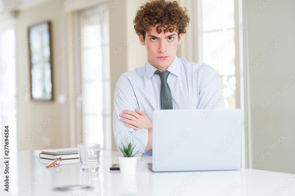 Young business man working with computer laptop at the office skeptic and nervous, disapproving expression on face with crossed arms. Negative person.