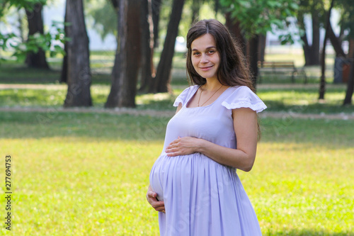 Portrait of beautiful young woman supporting her big pregnant belly with both hands.
