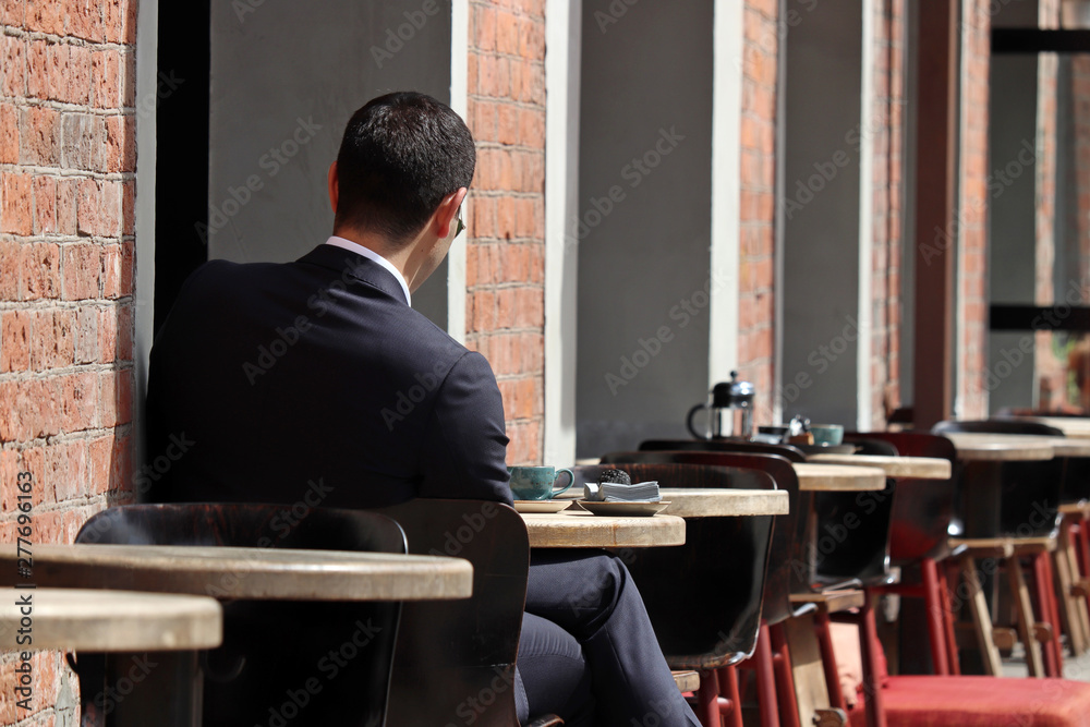 Stylish man in a business suit sitting at a table in street cafe. Concept of lunch alone, waiting for a date or business meeting, coffee break Stylish man in a business suit sitting at a table in street cafe. Concept of lunch alone, waiting for a date or business meeting, coffee break