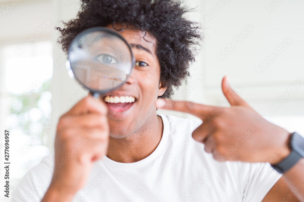 African American man looking through magnifying glass very happy pointing with hand and finger African American man looking through magnifying glass very happy pointing with hand and finger