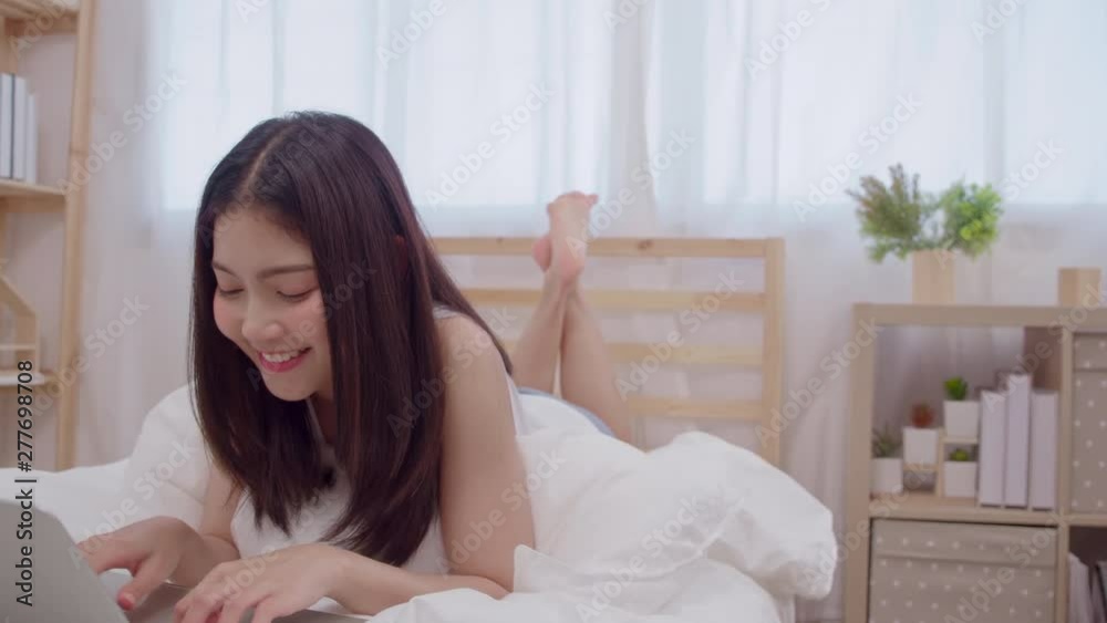 Young business freelance Asian woman working on laptop checking social media while lying on the bed when relax in bedroom at home. Lifestyle women at house concept. Young business freelance Asian woman working on laptop checking social media while lying on the bed when relax in bedroom at home. Lifestyle women at house concept.