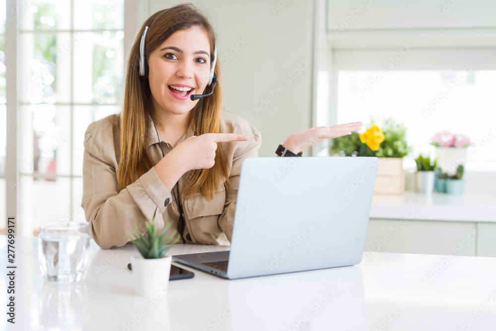 Beautiful young operator woman working with laptop and wearing headseat amazed and smiling to the camera while presenting with hand and pointing with finger.